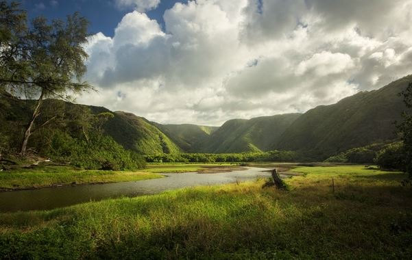 Sunlit valley with a river and clouds in Polulu Valley Hawaii